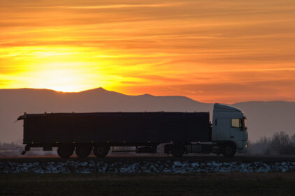 Semi-truck with cargo trailer driving on highway hauling goods in evening.